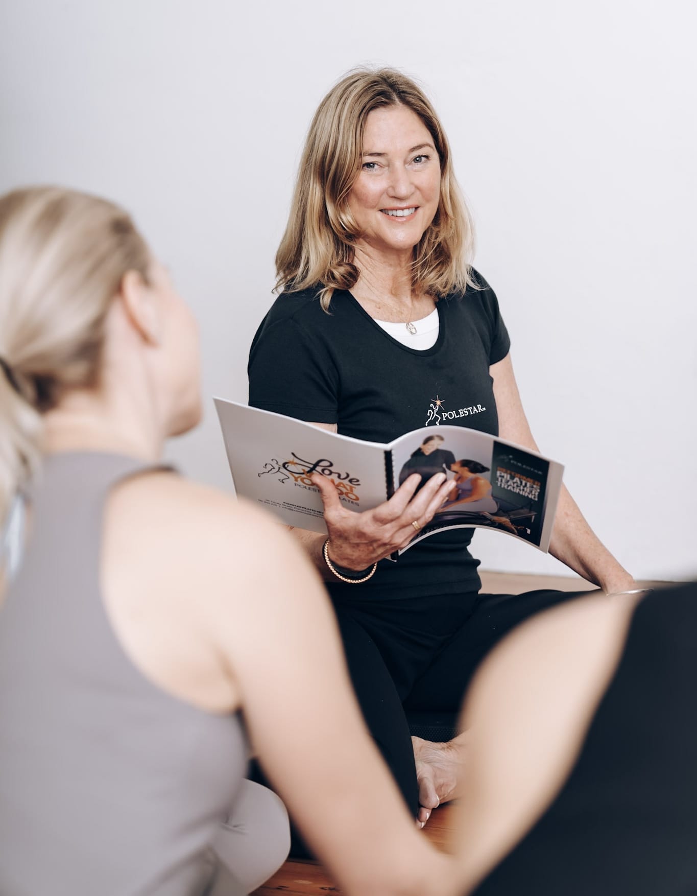 Polestar Pilates NZ licensee Maree with Manual and Tamsin Polestar Pilates instructor demonstrating a teacher training manual to a student during a Pilates certification course in New Zealand.