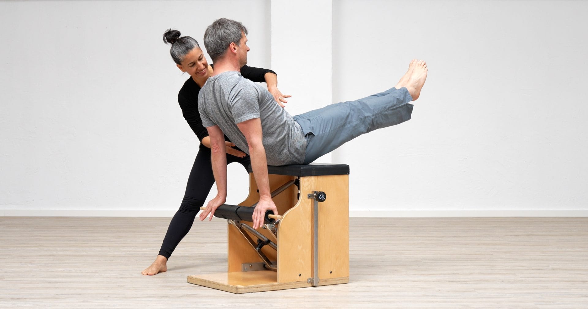 Polestar Senior Educator Christi Idavoy instructing a student on the Pilates Chair in a teaser exercise.